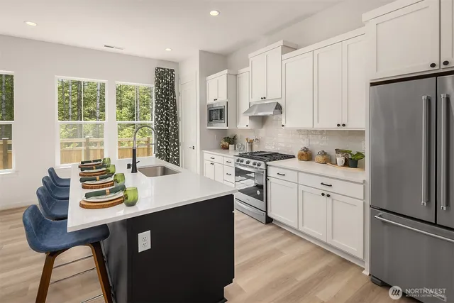 a kitchen with stainless steel appliances kitchen island granite countertop a sink a stove a refrigerator and white cabinets with wooden floor