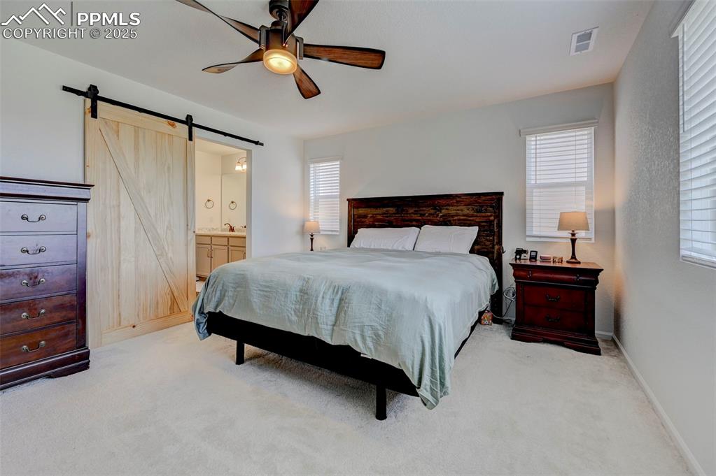 6237 Bodacious Circle Colorado Springs, CO 80923 - Photo 18 of 33 Bedroom featuring a barn door, light colored carpet, a ceiling fan, and ensuite bathroom