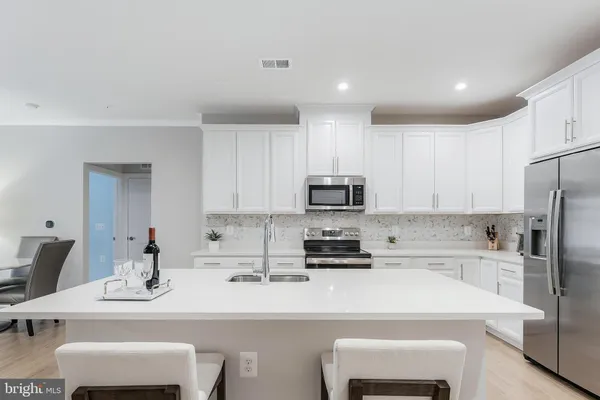 a kitchen with stainless steel appliances a sink a stove a refrigerator and white cabinets with wooden floor