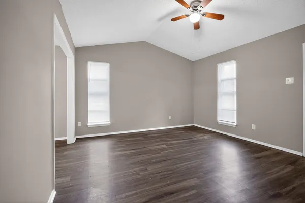 an empty room with wooden floor chandelier fan and windows
