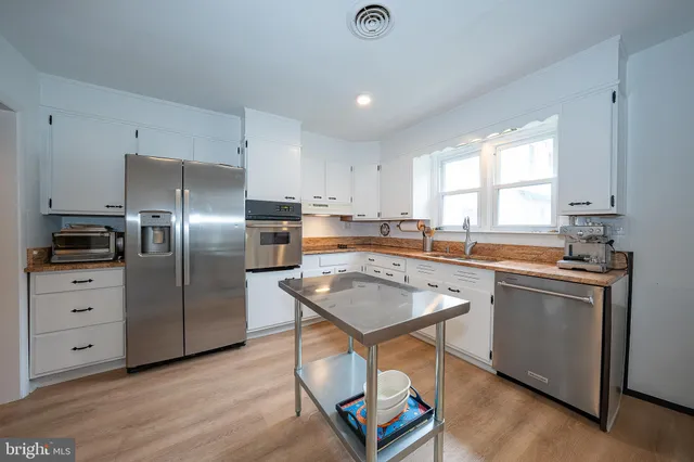 a kitchen with stainless steel appliances granite countertop a refrigerator a sink a stove and white cabinets