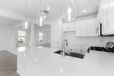 a large white kitchen with granite countertop a stove a sink a refrigerator and white cabinets with wooden floor