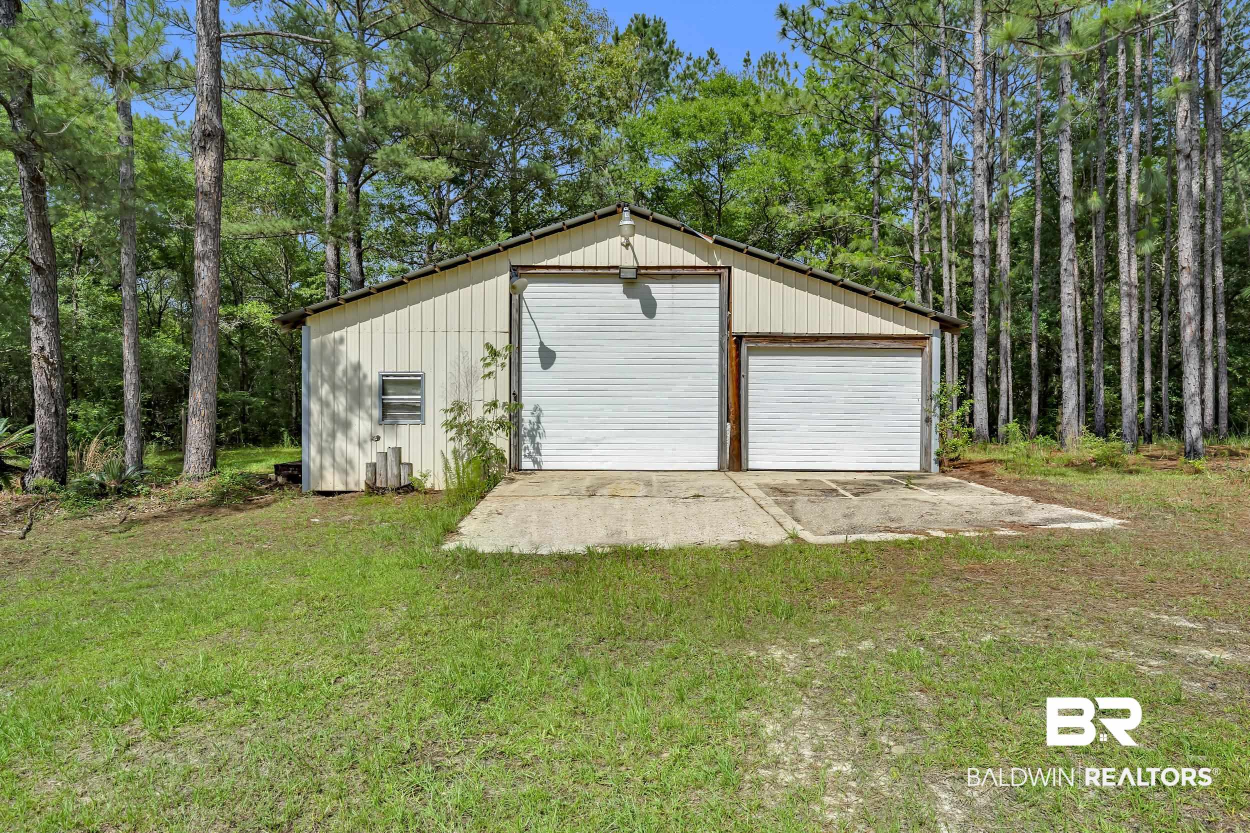 14960 Howells Ferry Road Wilmer, AL 36587 - Photo 22 of 22 Metal-sided utility building featuring two garage doors, a concrete pad, and a side window