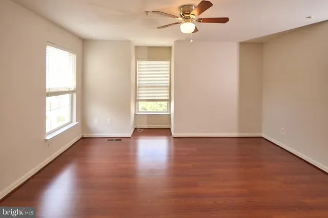 an empty room with wooden floor fan and windows