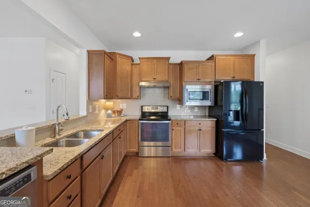 a kitchen with stainless steel appliances granite countertop a refrigerator a sink dishwasher a stove with wooden cabinets and floor