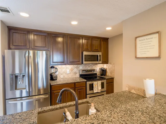 a kitchen with stainless steel appliances granite countertop a refrigerator a stove top oven and a sink