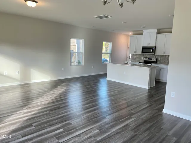 a view of kitchen and empty room with wooden floor