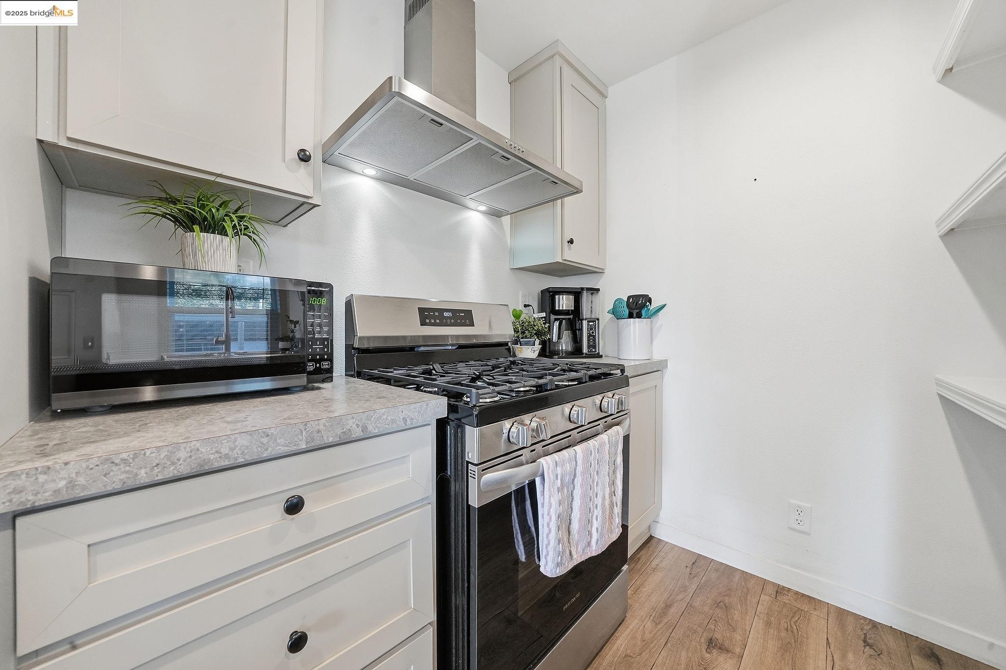 150 Clinton Road Jackson, CA 95642 - Photo 25 of 44 Kitchen with appliances with stainless steel finishes, wall chimney exhaust hood, light wood-style flooring, light countertops, and white cabinetry