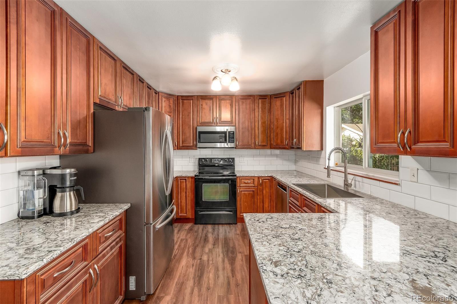 3217 South Stuart Street Denver, CO 80236 - Photo 3 of 30 a kitchen with granite countertop wooden cabinets a refrigerator stove top oven with granite countertops and wooden floor