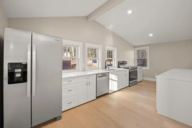 a large kitchen with a refrigerator a sink dishwasher a oven with white cabinets and wooden floor