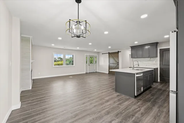 a view of an empty room and kitchen with wooden floor