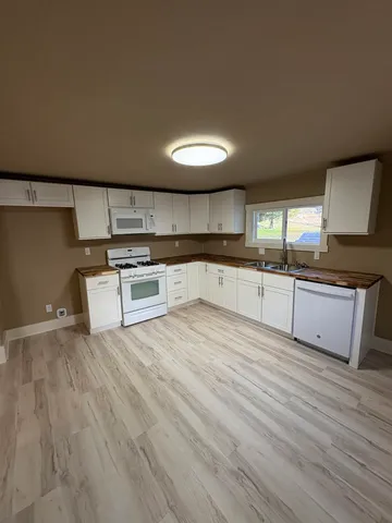 a large white kitchen with stainless steel appliances granite countertop a stove and a sink