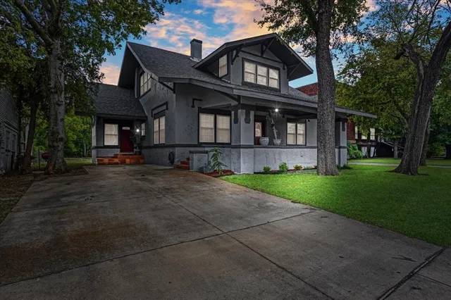 a view of a brick house with a large windows and a yard with plants and large trees