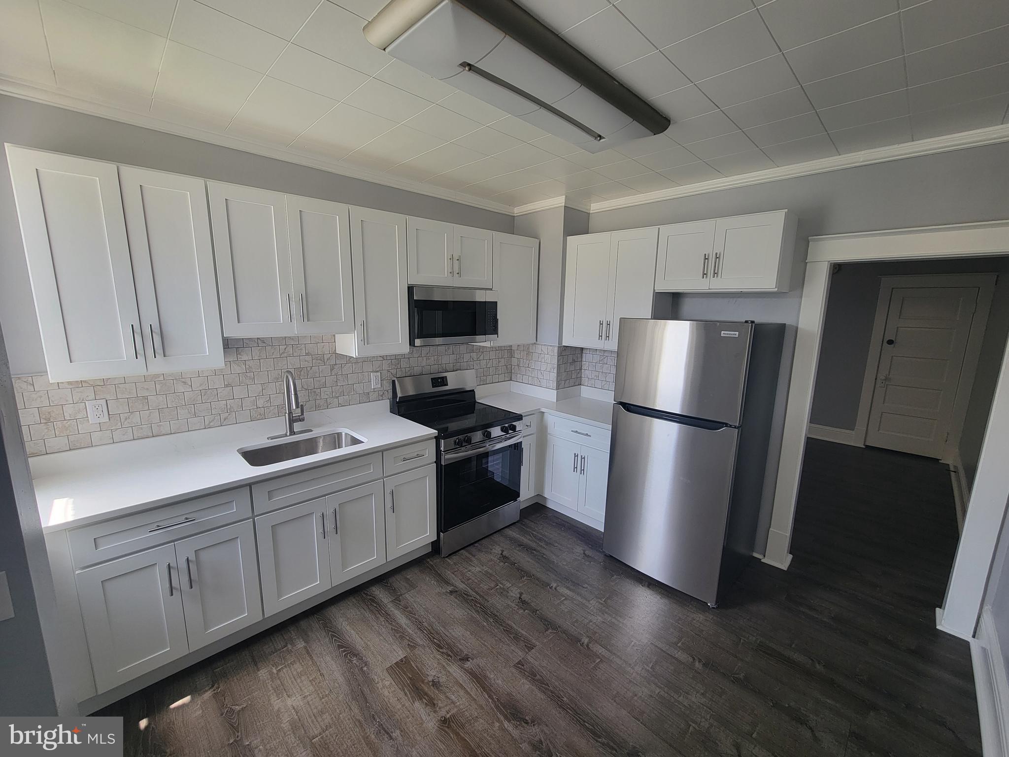 6757 Woodley Road Dundalk, MD 21222 - Photo 3 of 27 a kitchen with a refrigerator a sink a stove a microwave and wooden floors