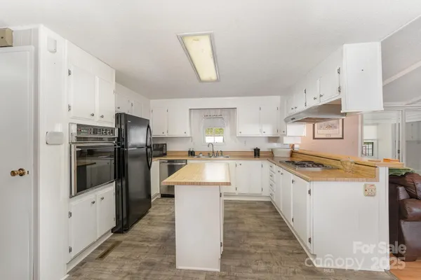 a large kitchen with stainless steel appliances kitchen island a stove a sink dishwasher a refrigerator and white cabinets with wooden floor