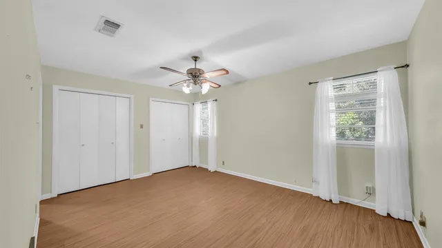 an empty room with wooden floor chandelier fan and windows