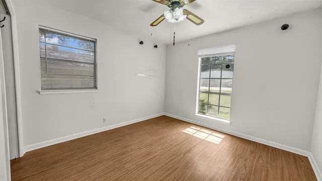 an empty room with wooden floor chandelier fan and windows