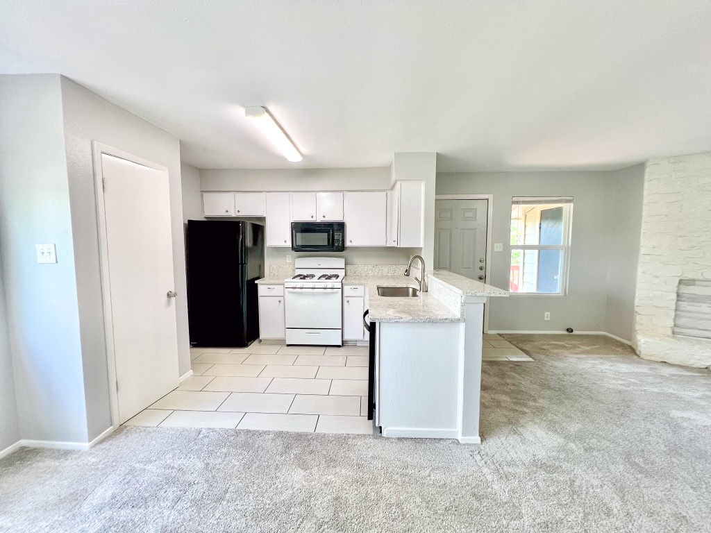 9703 Roxanna Drive, Unit D Austin, TX 78748 - Photo 19 of 24 Kitchen with black appliances, light carpet, white cabinets, and light tile patterned flooring