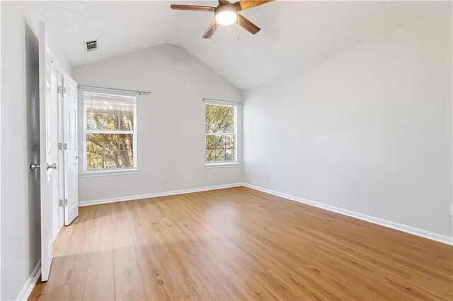an empty room with wooden floor chandelier fan and windows