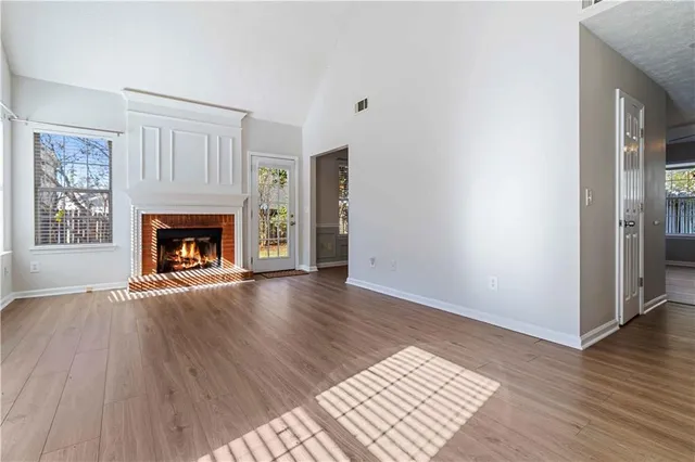 an empty room with wooden floor fireplace and windows