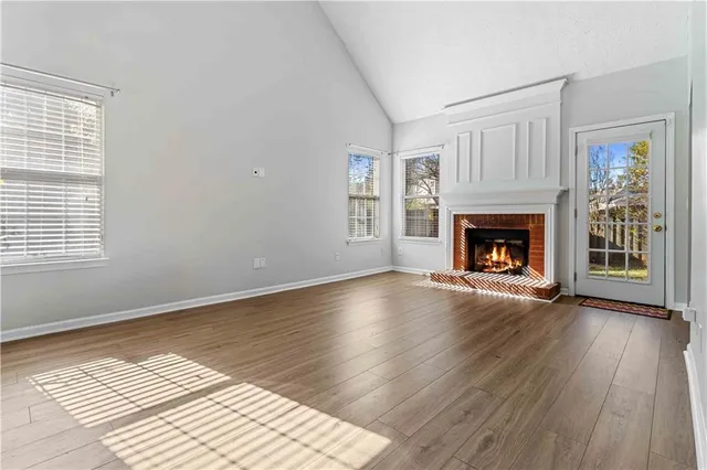 a view of an empty room with wooden floor fireplace and a window