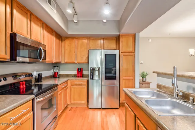 a kitchen with stainless steel appliances granite countertop a refrigerator a sink dishwasher a stove with wooden cabinets and floor