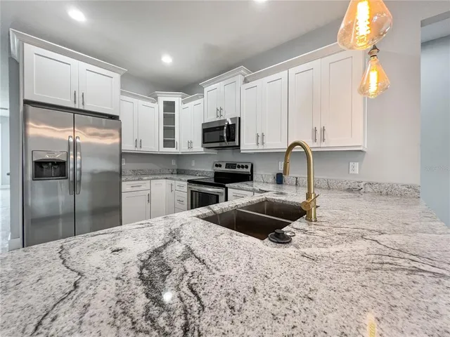 a kitchen with granite countertop a refrigerator a sink a stove a microwave and wooden cabinets