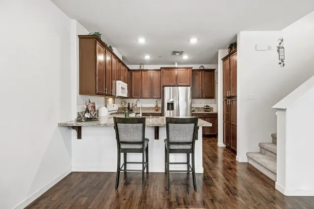 a kitchen with stainless steel appliances kitchen island granite countertop a refrigerator a stove a sink and a dining table with wooden floor