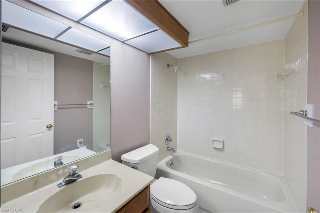 5857 Rattlesnake Hammock Road, Unit 101 Naples, FL 34113 - Photo 15 of 19 Bathroom featuring a built-in bathtub with shower, white tile surround, and an integrated toilet