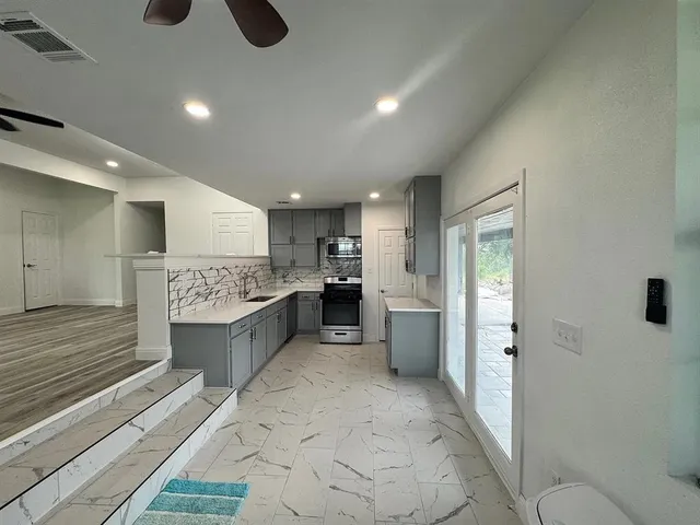 a large room with stainless steel appliances kitchen island granite countertop a refrigerator stove oven with white cabinets and wooden floor