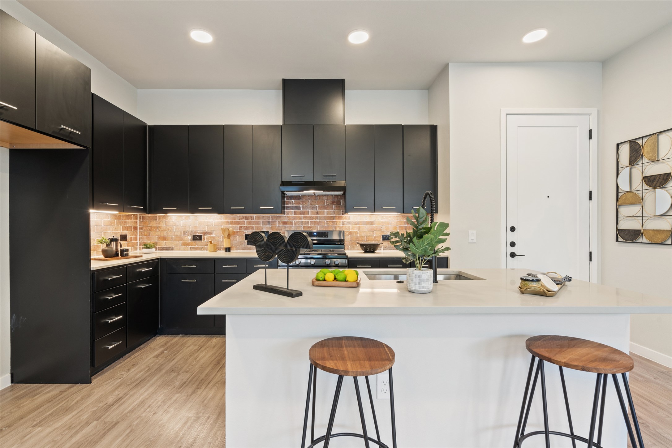 4510 Terry-O Lane, Unit 341 Austin, TX 78745 - Photo 5 of 40 Modern kitchen featuring dark cabinetry, a light-colored island with a sink, a brick-style backsplash, and recessed lighting