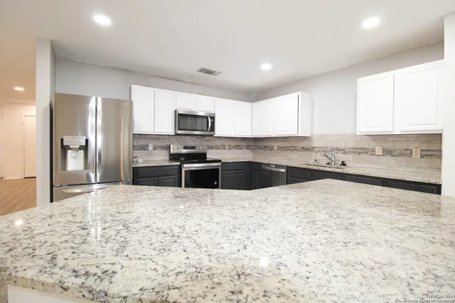 a large kitchen with granite countertop a stove a sink a microwave a counter space and cabinets