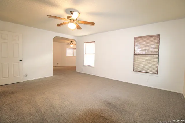 an empty room with chandelier fan and windows