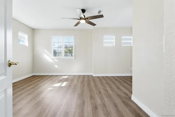 an empty room with wooden floor fan and windows