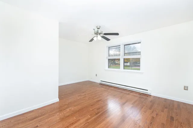 an empty room with wooden floor chandelier fan and windows