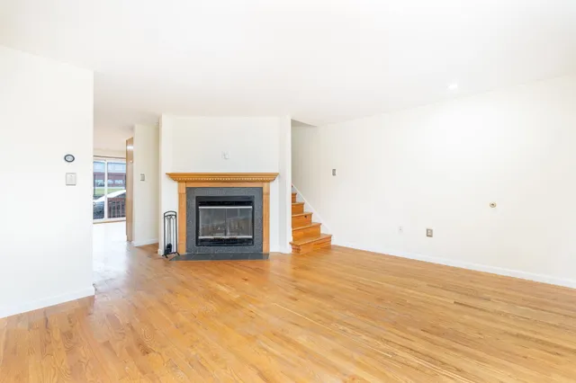 a view of an empty room with wooden floor fireplace and a window
