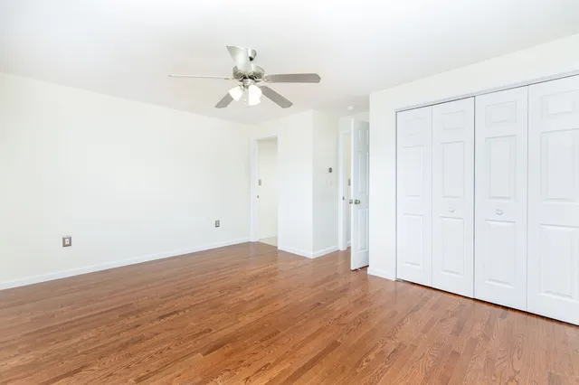 an empty room with wooden floor fan and windows