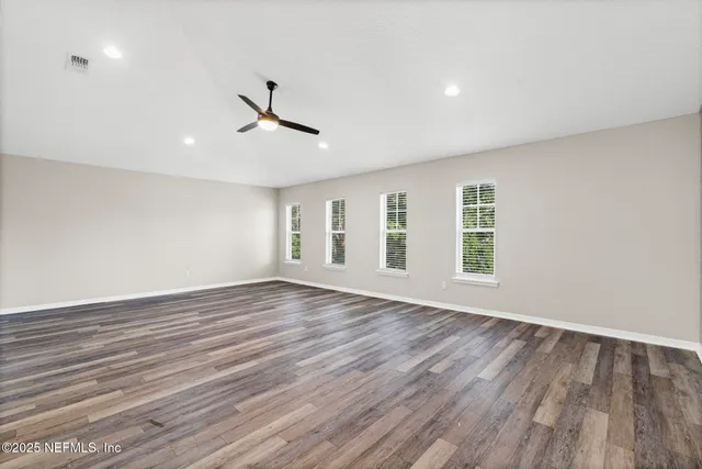 an empty room with wooden floor ceiling fan and windows