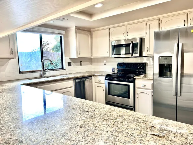 a kitchen with stainless steel appliances kitchen island granite countertop a stove a sink and a refrigerator