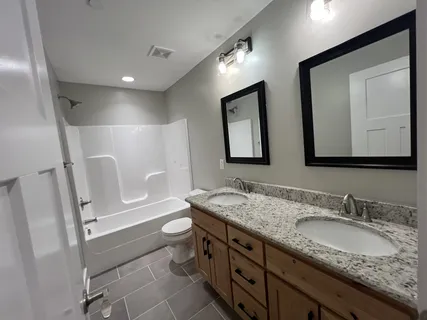 a bathroom with a granite countertop toilet a double vanity sink and a mirror