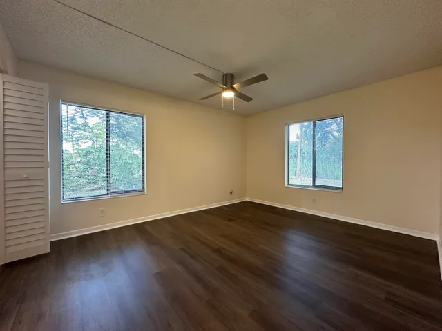 an empty room with wooden floor chandelier fan and windows