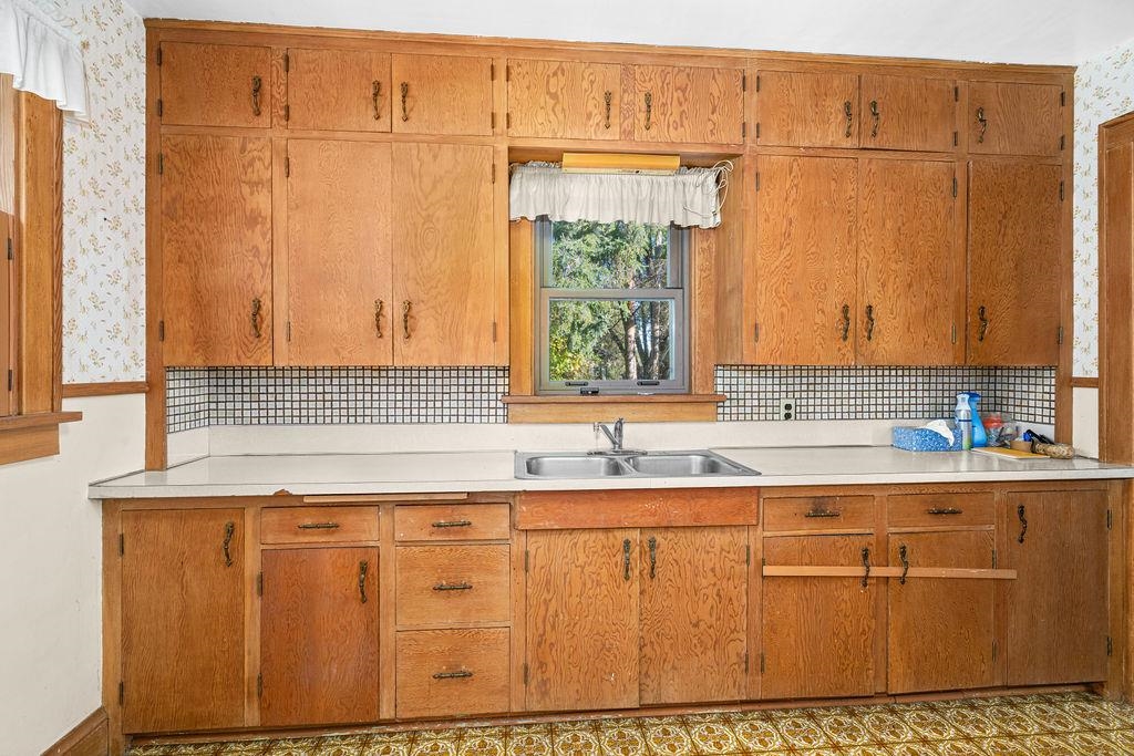 434 12th Street Cloquet, MN 55720 - Photo 8 of 22 Kitchen featuring light countertops, brown cabinets, decorative backsplash, and wallpapered walls