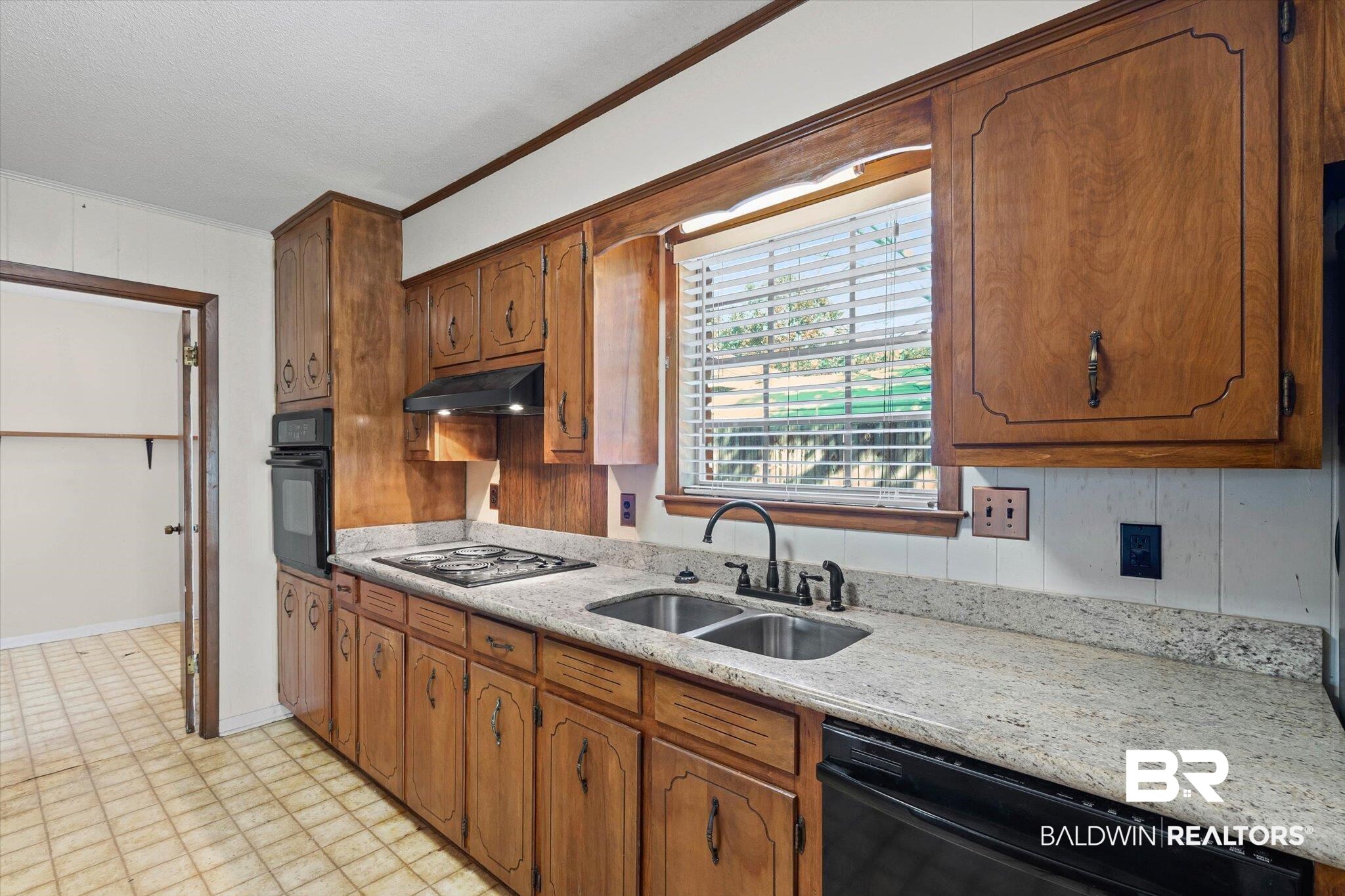 6300 Christopher Drive North Mobile, AL 36609 - Photo 8 of 22 Kitchen with black appliances, light stone counters, ornamental molding, brown cabinetry, and under cabinet range hood