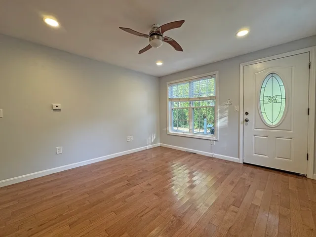 an empty room with wooden floor chandelier fan and windows