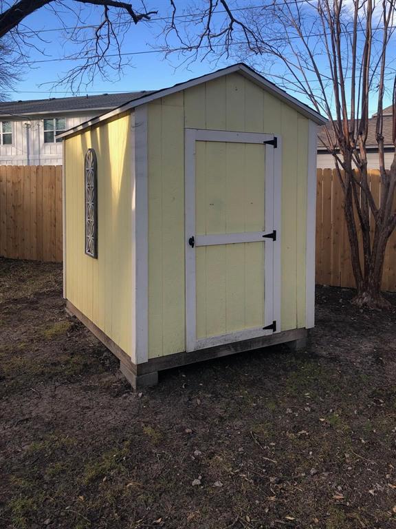 602 West 3rd Street Justin, TX 76247 - Photo 21 of 22 Detached storage shed with pale yellow siding, white trim, a black shingled roof, and a decorative arched window accent