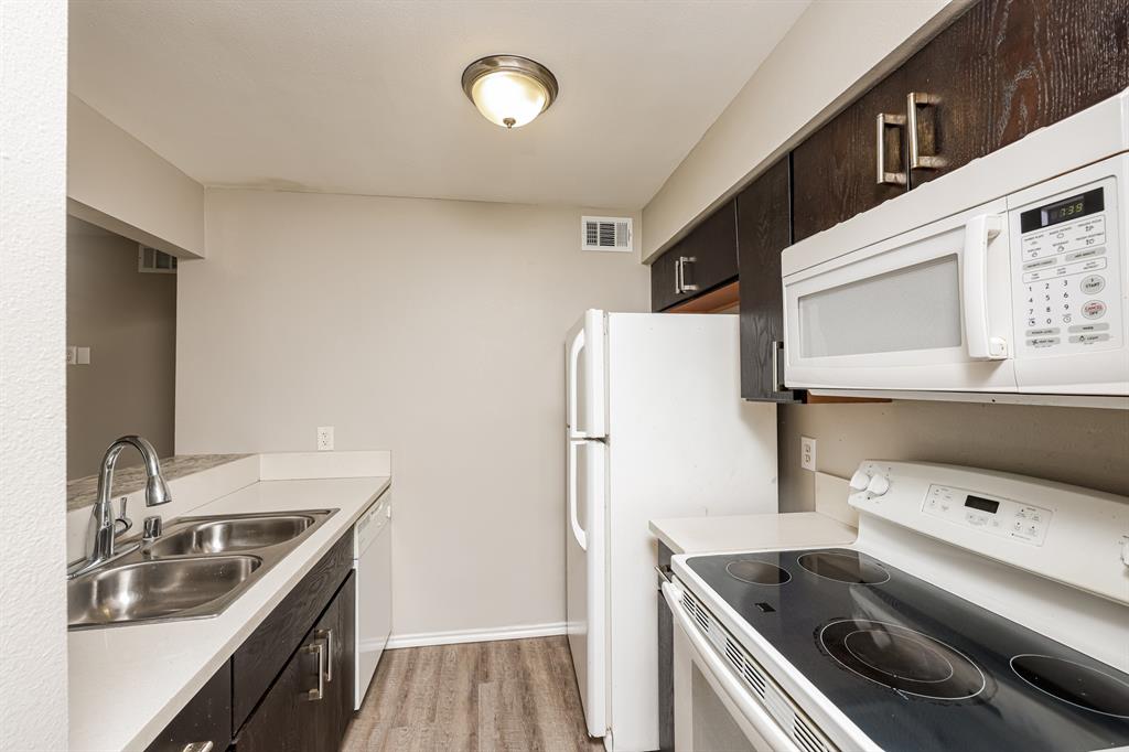 4622 Monarch Street, Unit 202 Dallas, TX 75204 - Photo 8 of 16 Kitchen featuring wood-finish flooring, dark cabinetry with contemporary pulls, a double basin stainless steel sink, light countertops, and white appliances including a refrigerator, dishwasher, stove, and microwave