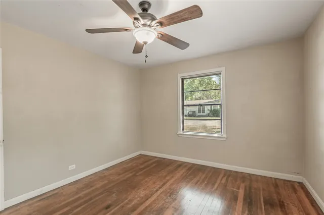 an empty room with wooden floor chandelier fan and windows