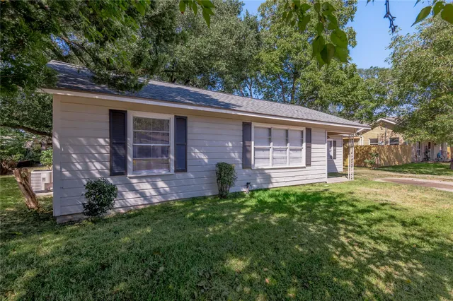 a view of a house with brick walls and a yard with plants and large trees