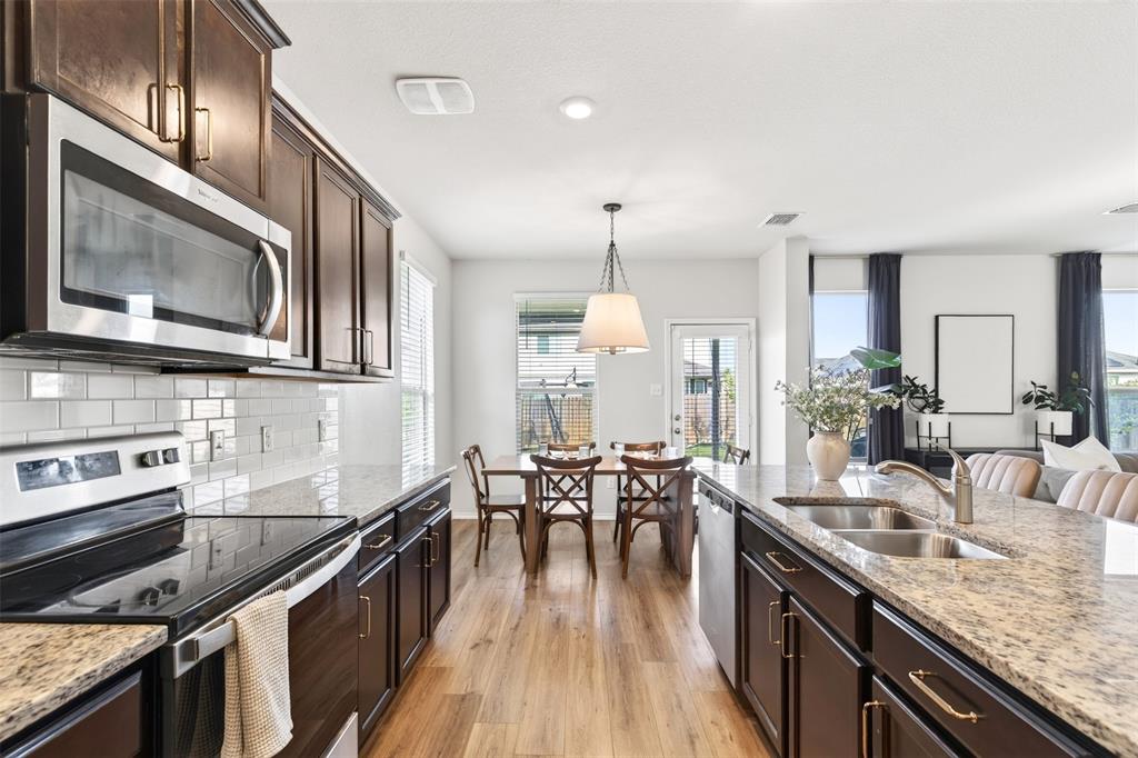 3105 Marston Road Lorena, TX 76655 - Photo 12 of 40 Modern kitchen featuring a large island with dual sinks, dark wood cabinetry, stainless steel appliances, white subway tile backsplash, and light-toned wood-finish flooring