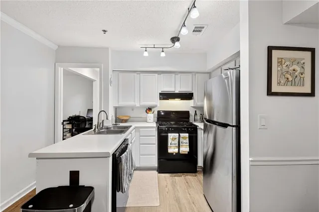 a kitchen with stainless steel appliances a refrigerator a sink a stove white cabinets and wooden floor